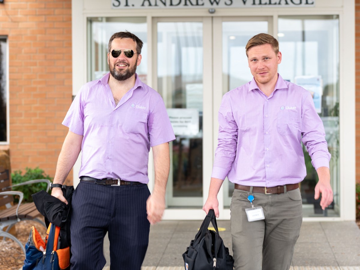 Two ClubIT engineers in branded shirts walking out of
               the main entrance of St Andrews in Ballina carrying tool bags after an onsite visit